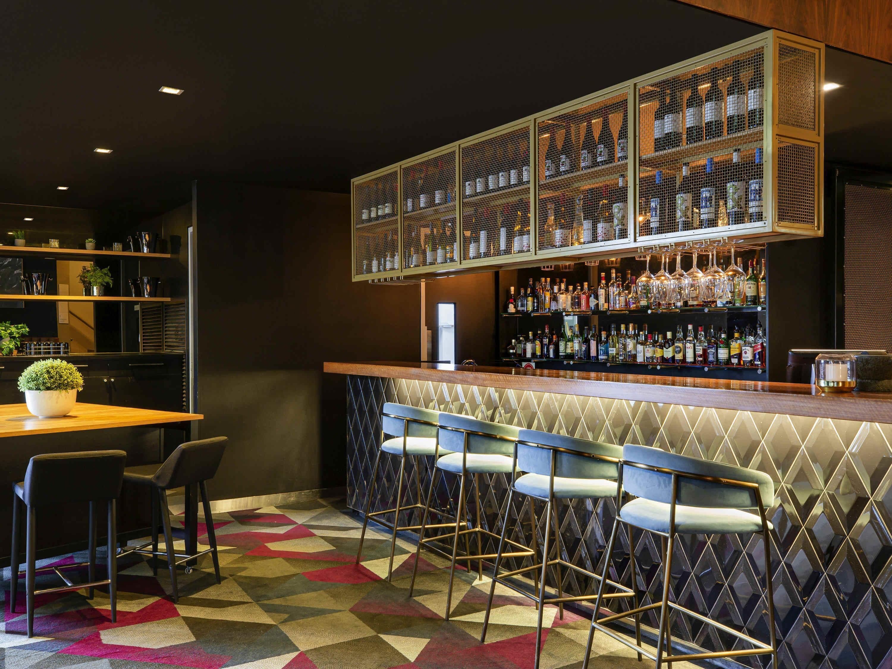 A bar area with a counter, stools, shelves with bottles, and a decorative plant.