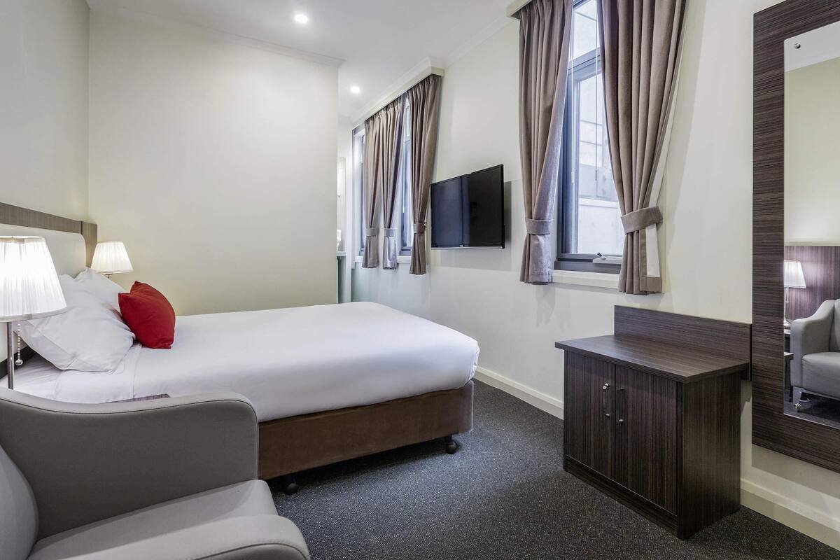 Ein Hotelzimmer mit Bett, Nachttischlampen, Fernseher, Schreibtisch und Stuhl.