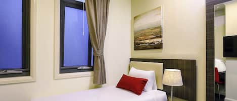 A hotel room with a bed, a nightstand, a lamp, a painting on the wall, and a large mirror.