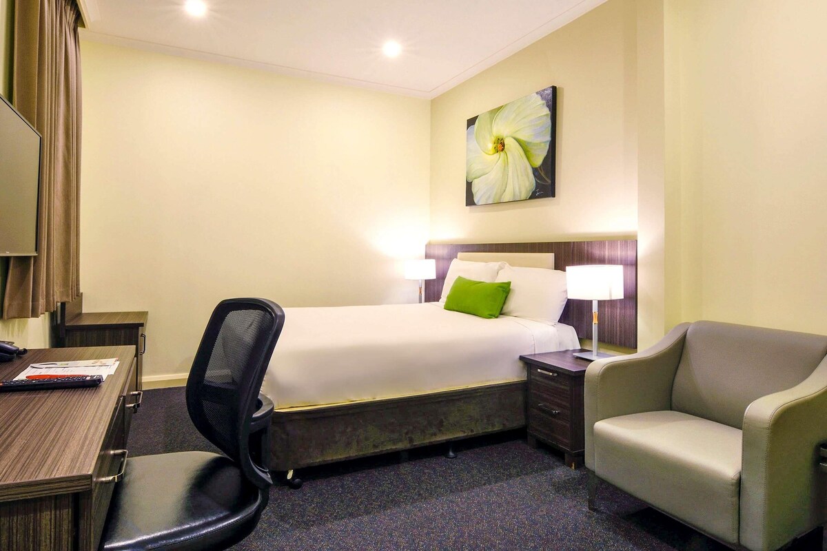 Une chambre d’hôtel comprenant un lit, un bureau avec une chaise, une table de chevet avec une lampe et un tableau au mur.