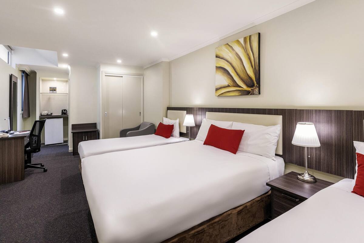 Ein Hotelzimmer mit einem großen Bett, einem Schreibtisch, einem Stuhl, einer kleinen Küchenzeile und einem Badezimmer.