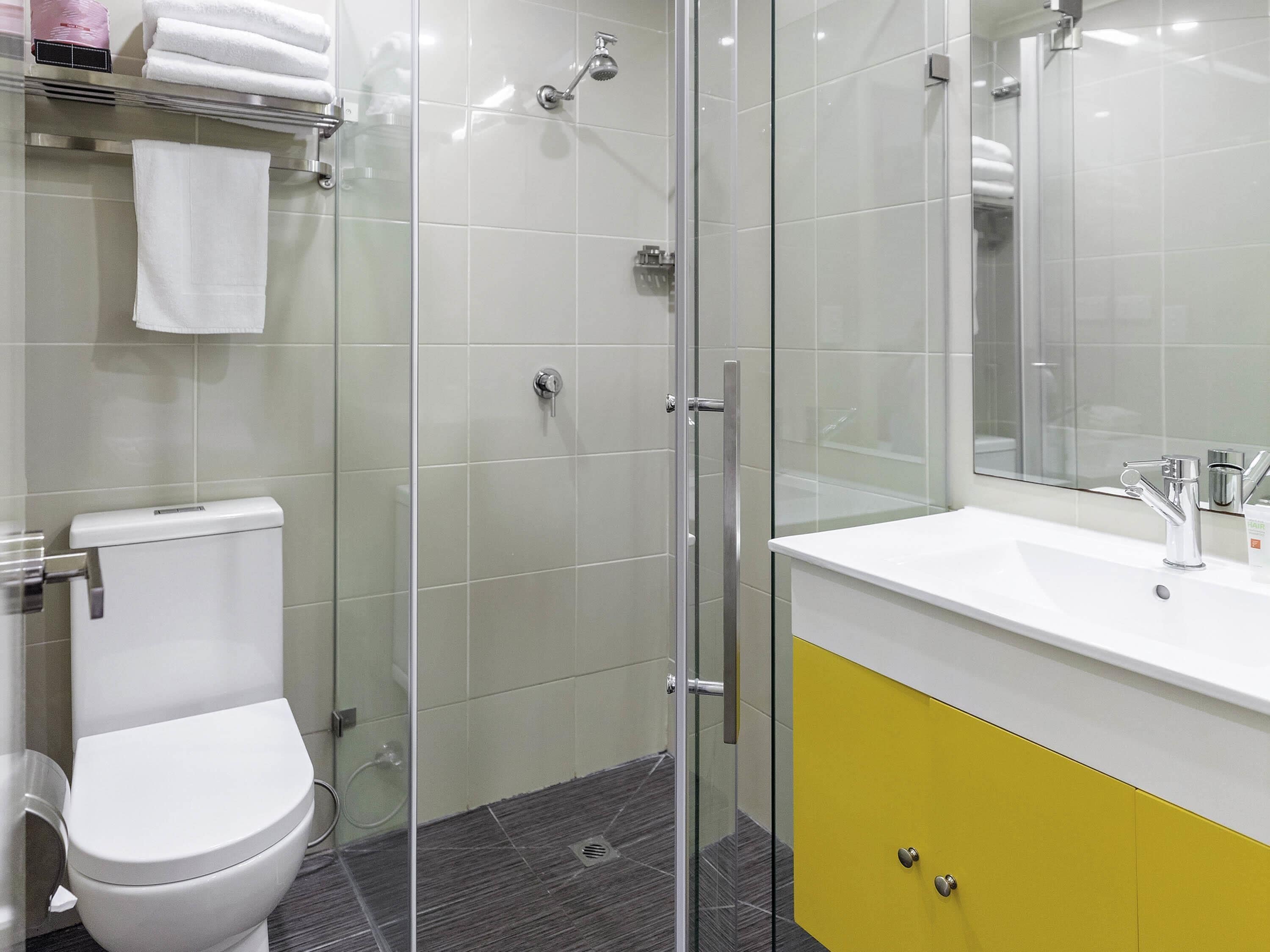 Un baño moderno con cabina de ducha de vidrio, inodoro blanco y tocador amarillo con espejo.