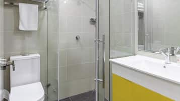 Un baño moderno con cabina de ducha de vidrio, inodoro blanco y tocador amarillo con espejo.