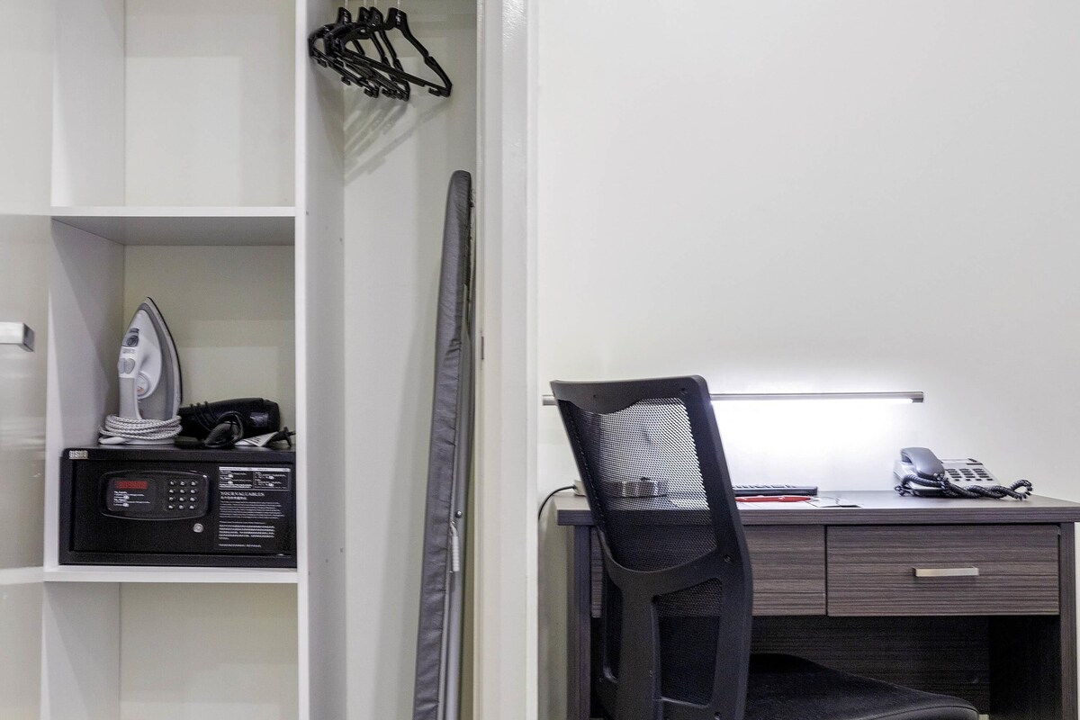 Une chambre d’hôtel équipée d’un bureau, d’une chaise, d’une planche à repasser et d’un porte-vêtements.