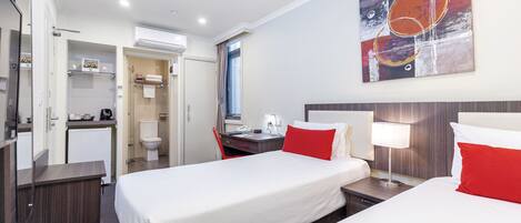 A hotel room with two beds, a desk, a chair, a small kitchenette, and a bathroom.