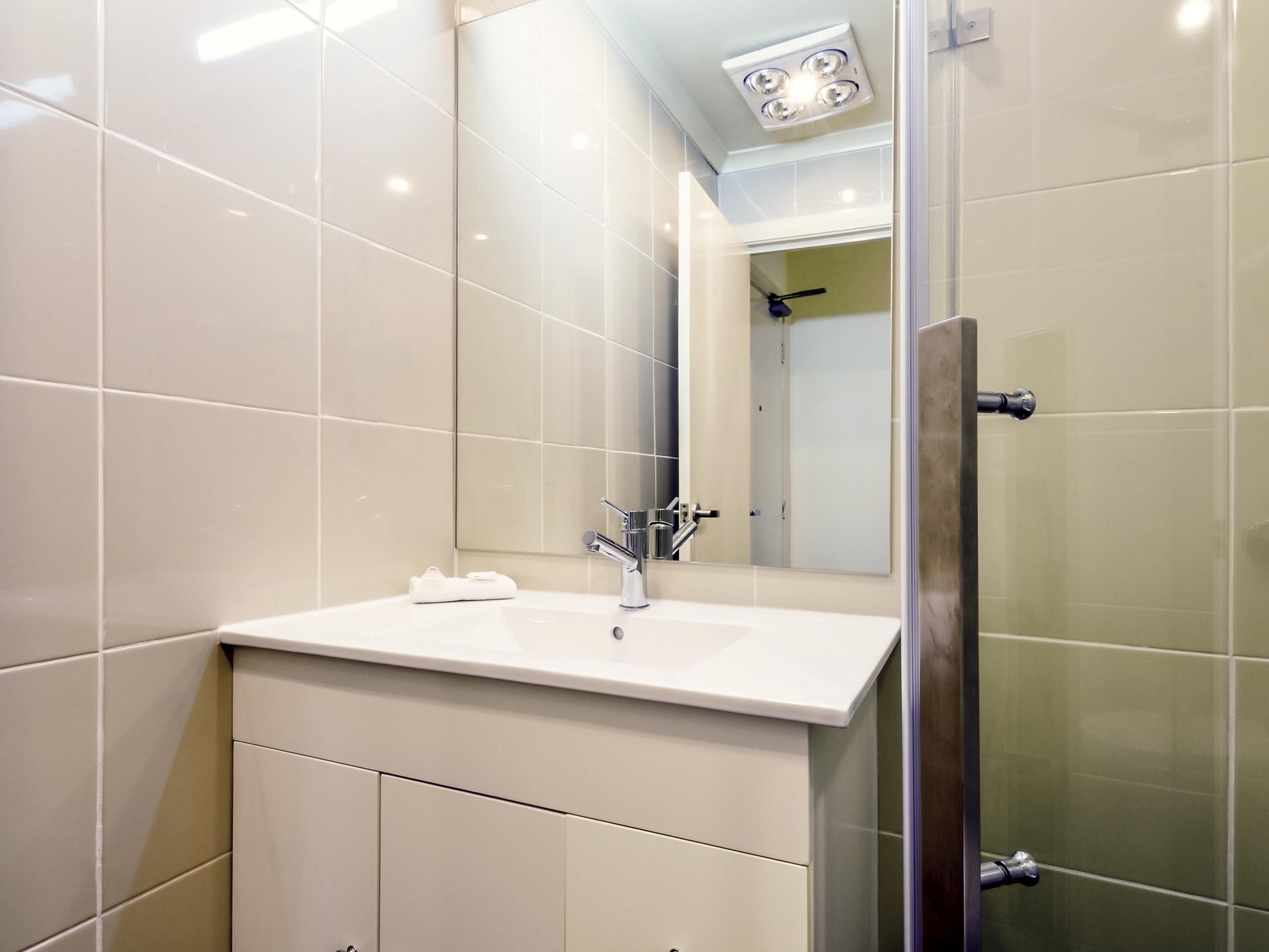 Un baño moderno con lavamanos blanco, un espejo y cabina de ducha de vidrio.