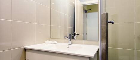 Un baño moderno con lavamanos blanco, un espejo y cabina de ducha de vidrio.