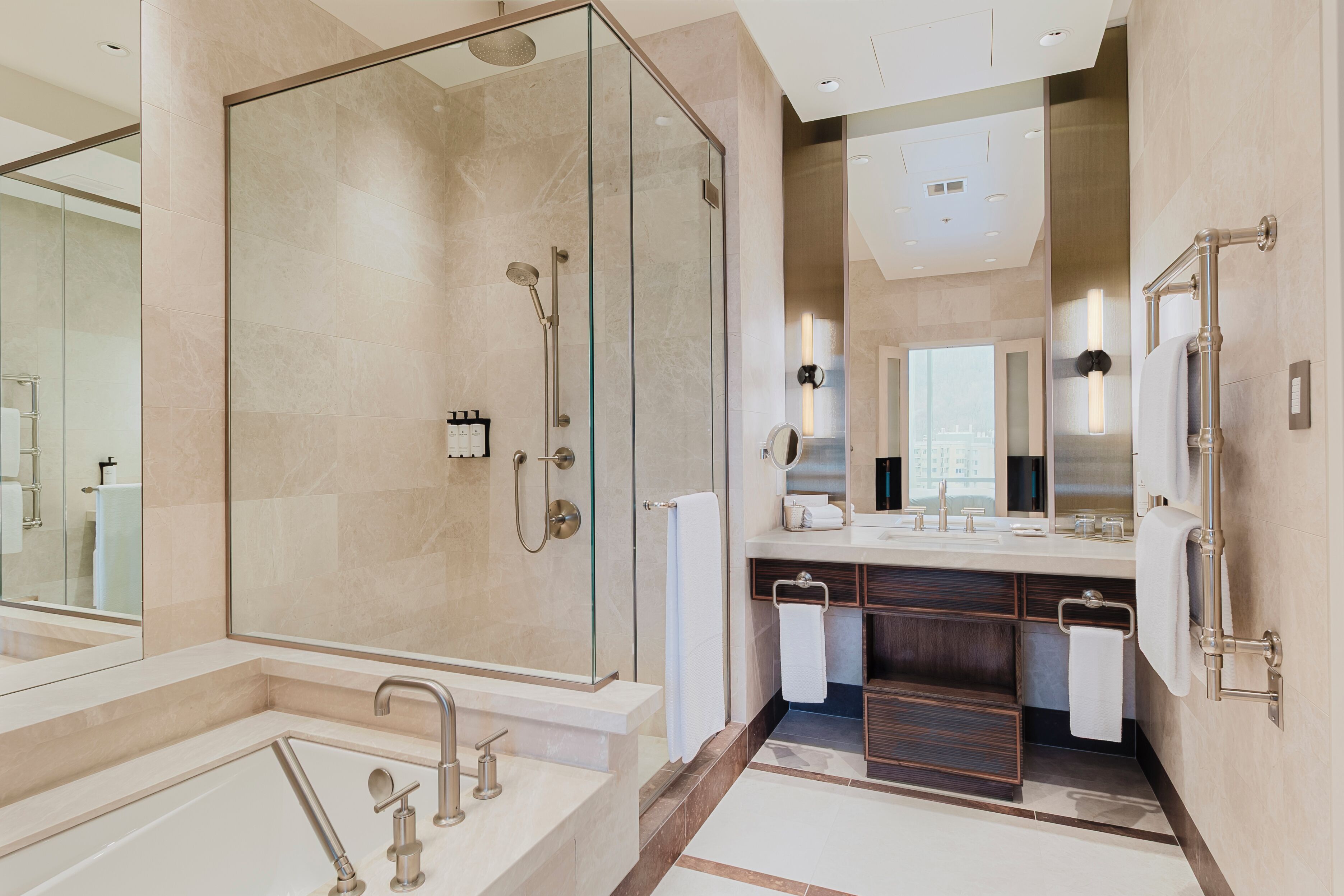 Un baño moderno con ducha envuelta en vidrio, un espejo grande y un tocador con lavabo y toallero.