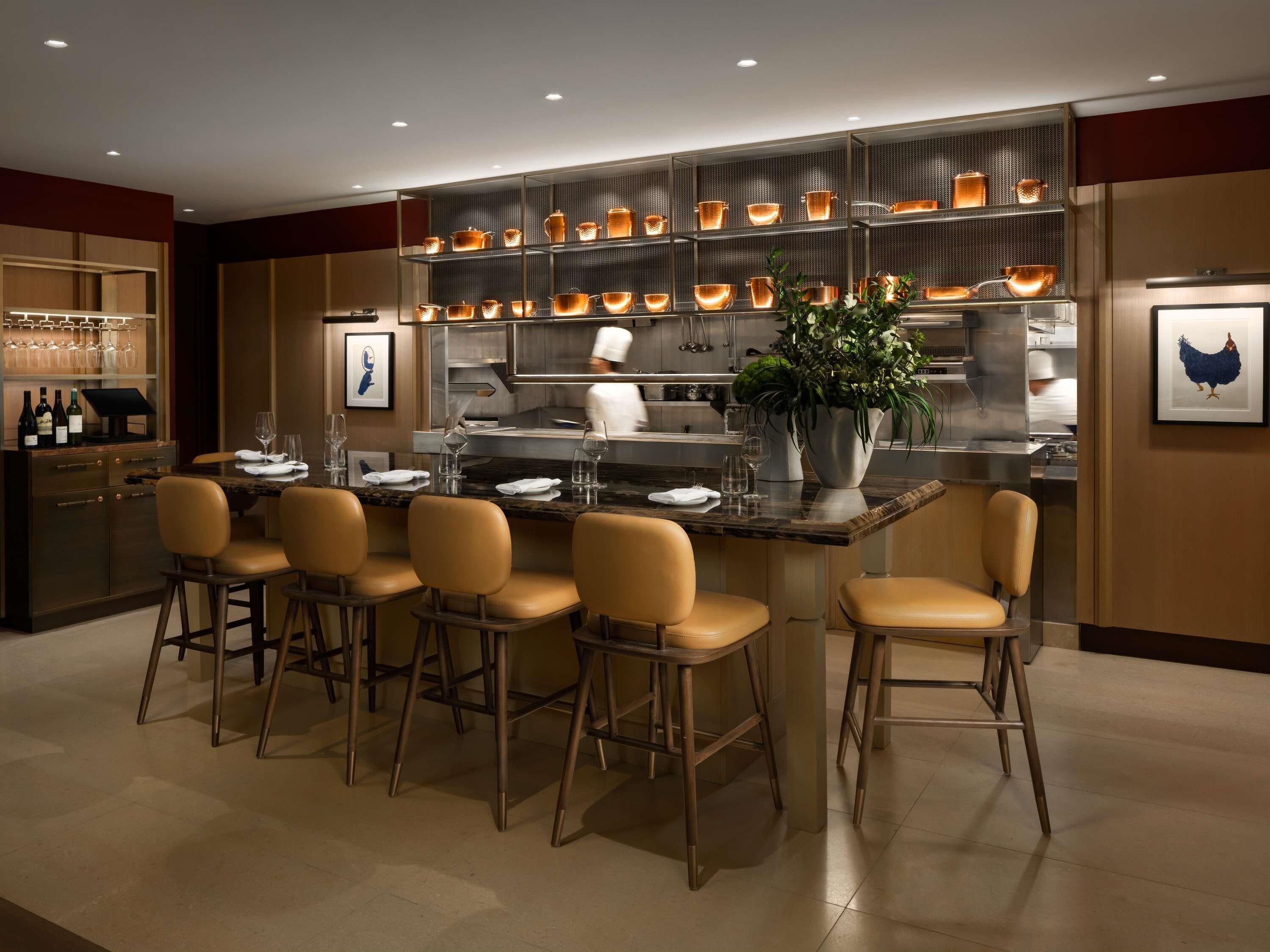 A modern bar area with a long counter, multiple stools, and a variety of copper cookware displayed on shelves.
