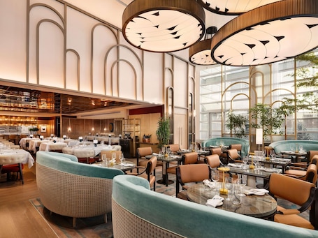 A spacious restaurant with high ceilings, modern chandeliers, and a variety of seating arrangements including booths and tables.. Sofitel Montreal Golden Mile