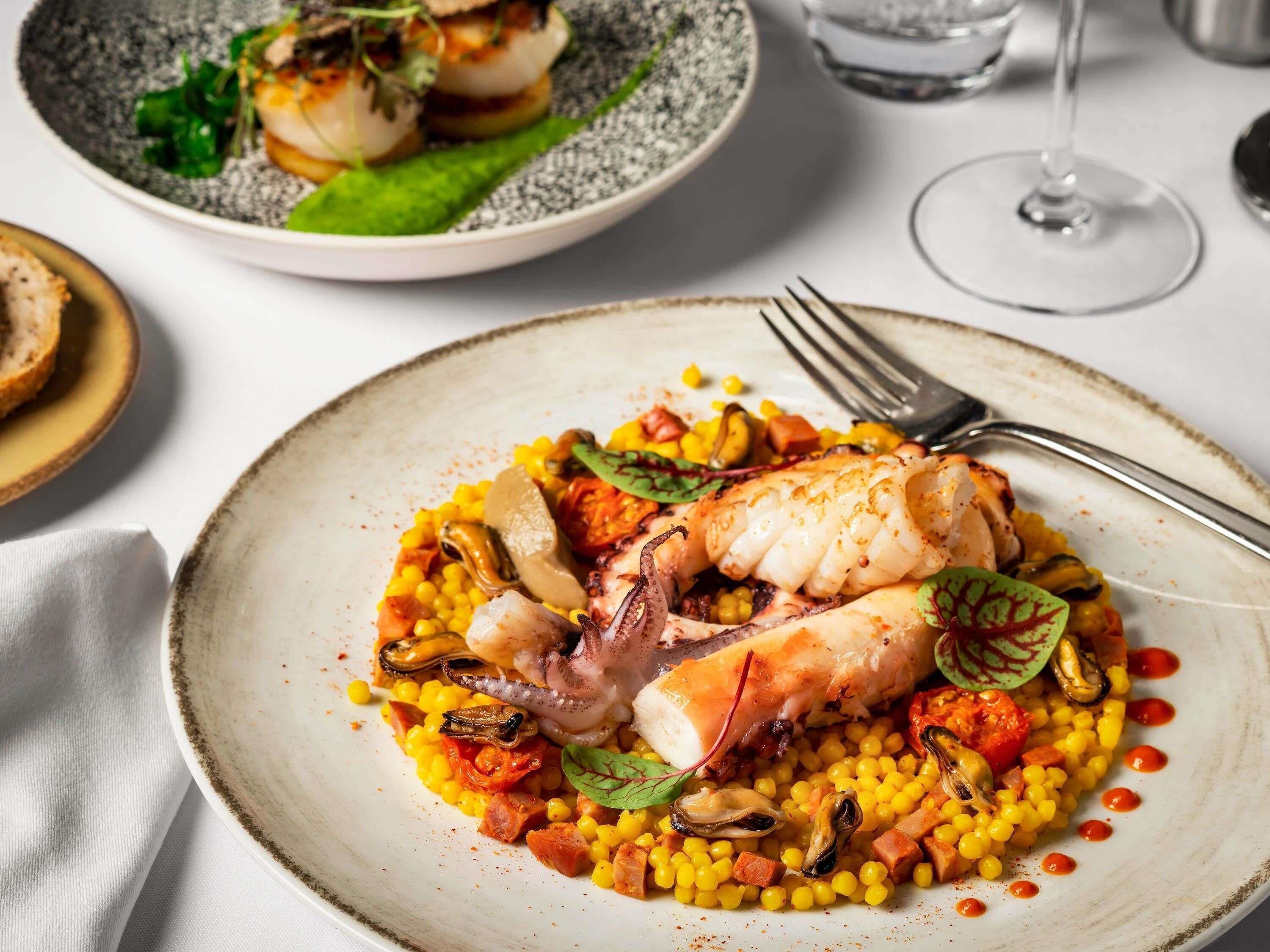 A plate of food with a fish and corn, accompanied by a fork and a glass of water.