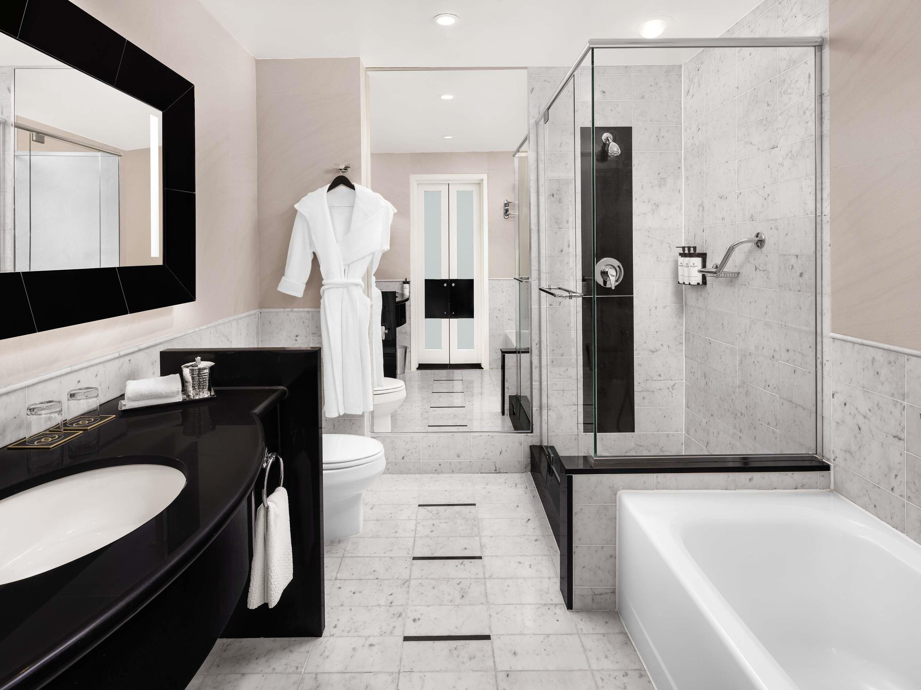 A modern bathroom with a large mirror, black vanity, white bathtub, and a glass-enclosed shower.