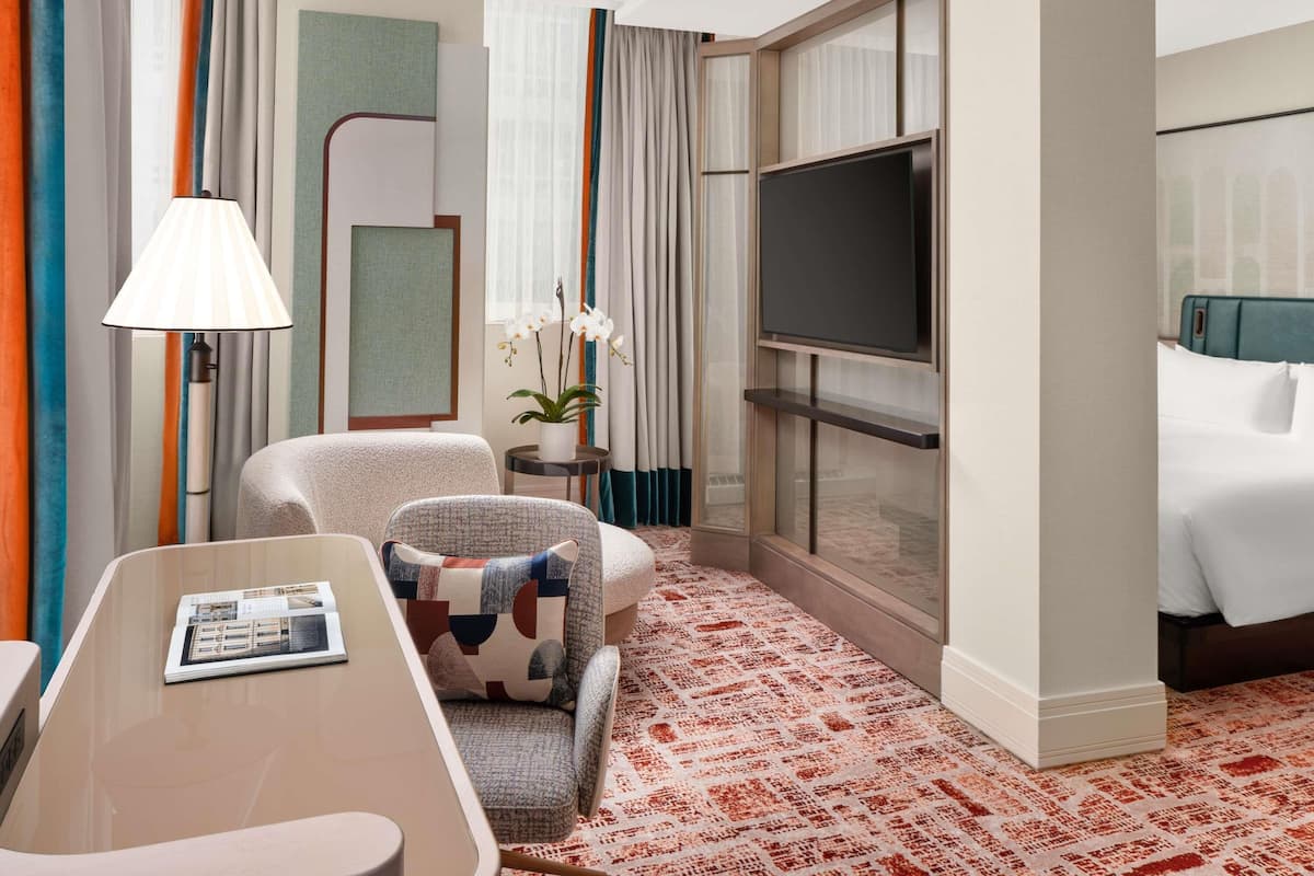 A hotel room with a bed, a TV, a sofa, a lamp, and a small table.