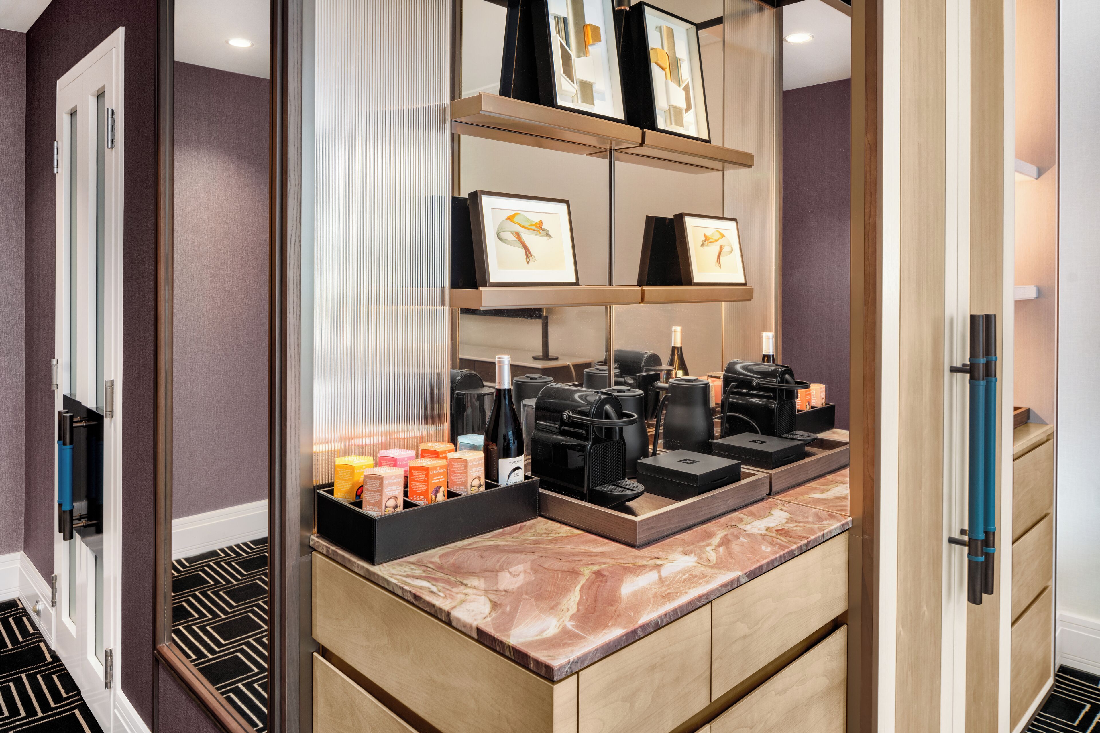 Habitación de hotel con encimera de mármol, obras de arte enmarcadas, cafetera y minibar.