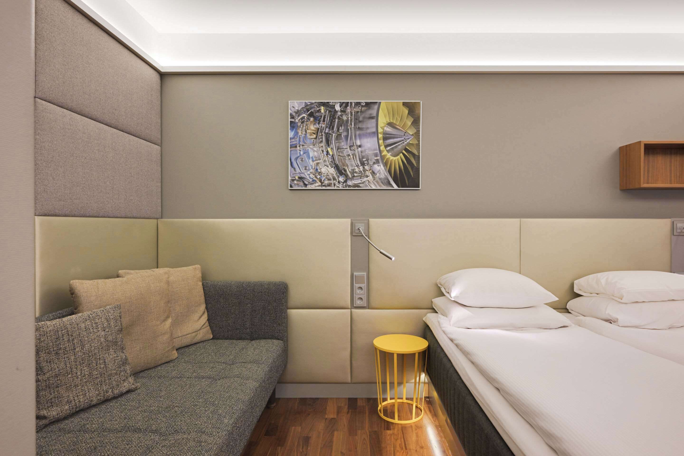 A modern hotel room with a sofa, a bed, a small round table, and a wall-mounted artwork.
