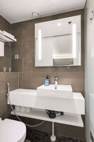Un baño moderno con un lavamanos blanco, un espejo encima y un cabezal de ducha.