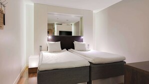 Ein modernes Hotelzimmer mit einem großen Bett, einem kleinen Nachttisch und einem Spiegel über dem Bett.