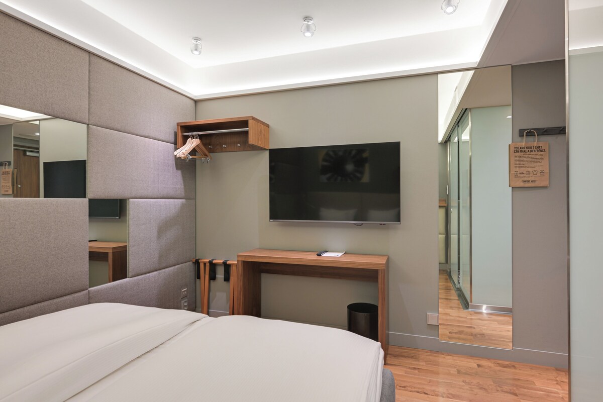 Une chambre moderne avec un grand lit, une table de chevet en bois, un téléviseur à écran plat et un miroir.