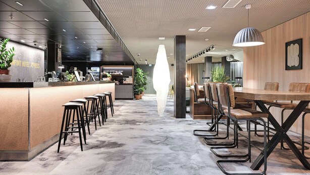 Eine moderne Hotelhalle mit Barbereich, Sitzgelegenheiten und einer großen dekorativen Leuchte.