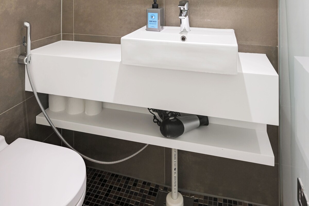 Une salle de bain moderne avec un lavabo blanc, un miroir au-dessus et une pomme de douche.