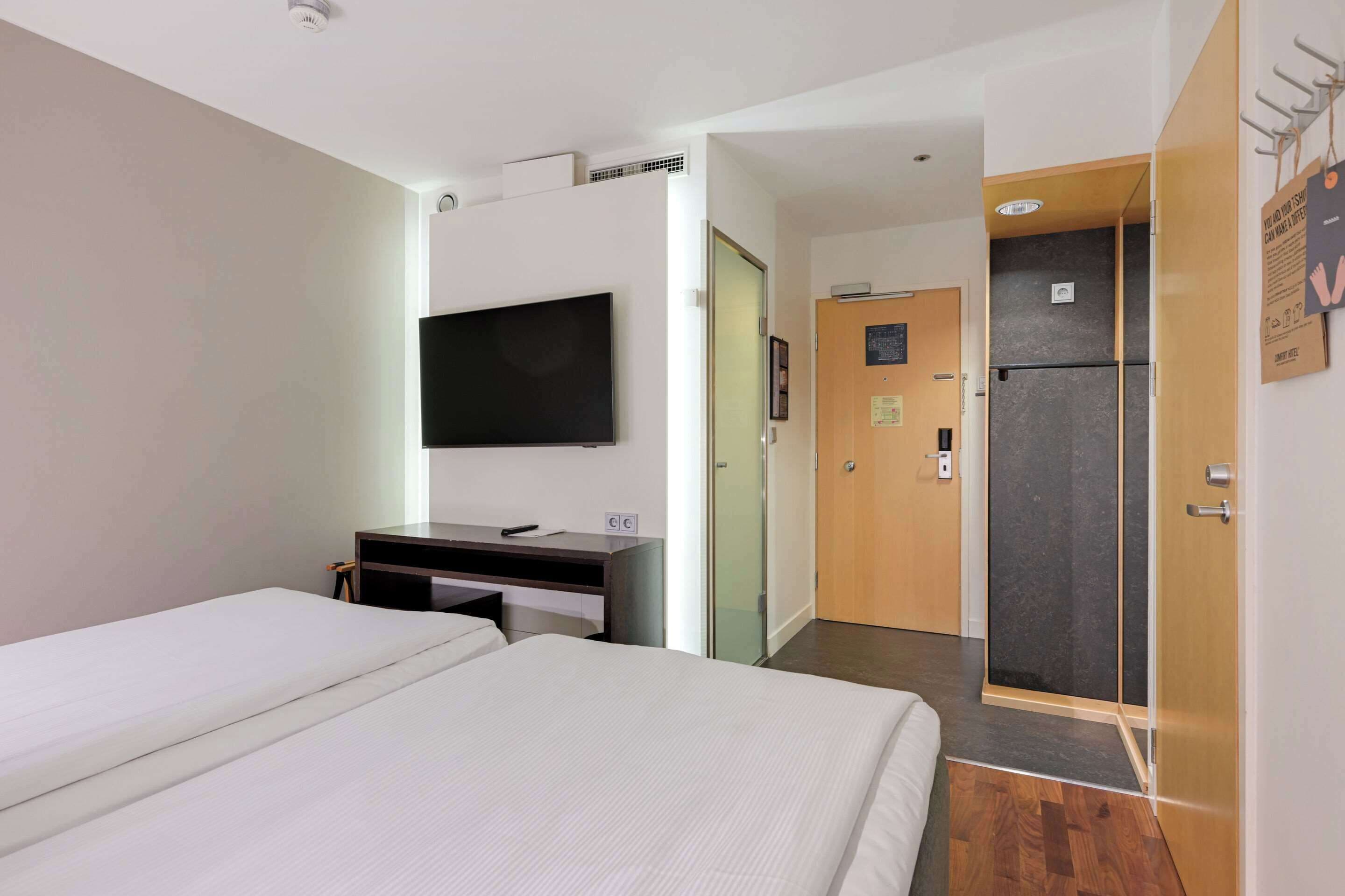 Ein Hotelzimmer mit Bett, Schreibtisch, Flachbildfernseher, Kühlschrank und Duschbereich.