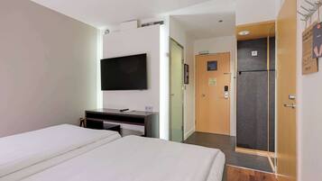 Ein Hotelzimmer mit Bett, Schreibtisch, Flachbildfernseher, Kühlschrank und Duschbereich.