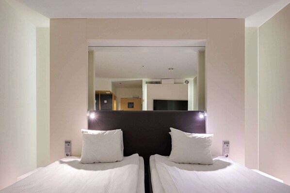 A hotel room with two single beds, a large mirror, and a door leading to a bathroom.