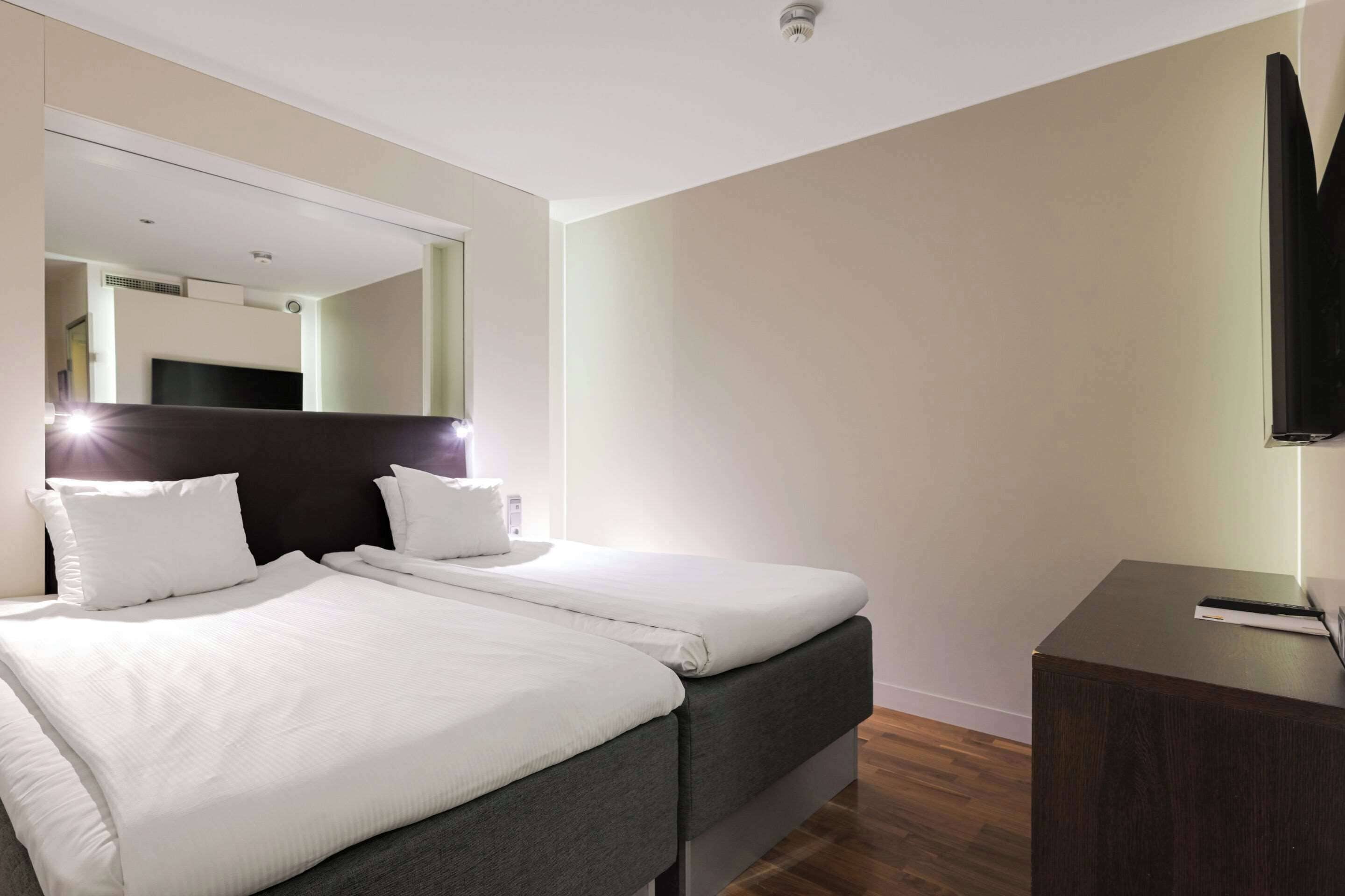 Hotellihuone, jossa on suuri sänky, yöpöytä, televisio ja peili.