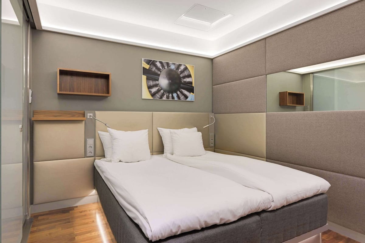 Un dormitorio moderno con una cama grande, cabecera, estante montado en la pared y lámpara en el techo.