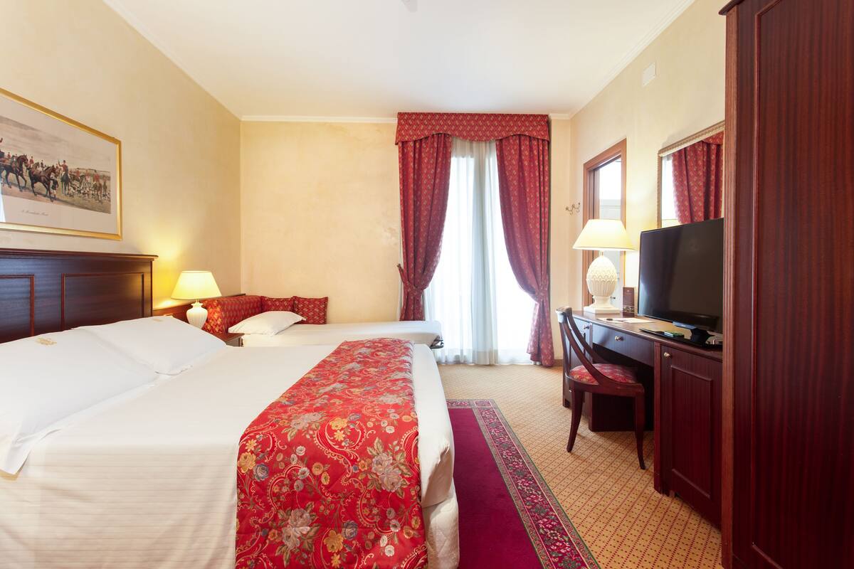 Ein Hotelzimmer mit einem großen Bett, einem Schreibtisch mit Fernseher, einem Sessel und einer Schreibtischlampe.