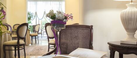 A well-lit room with a dining area, a wicker chair, a table with a book and a glass, and a lamp.