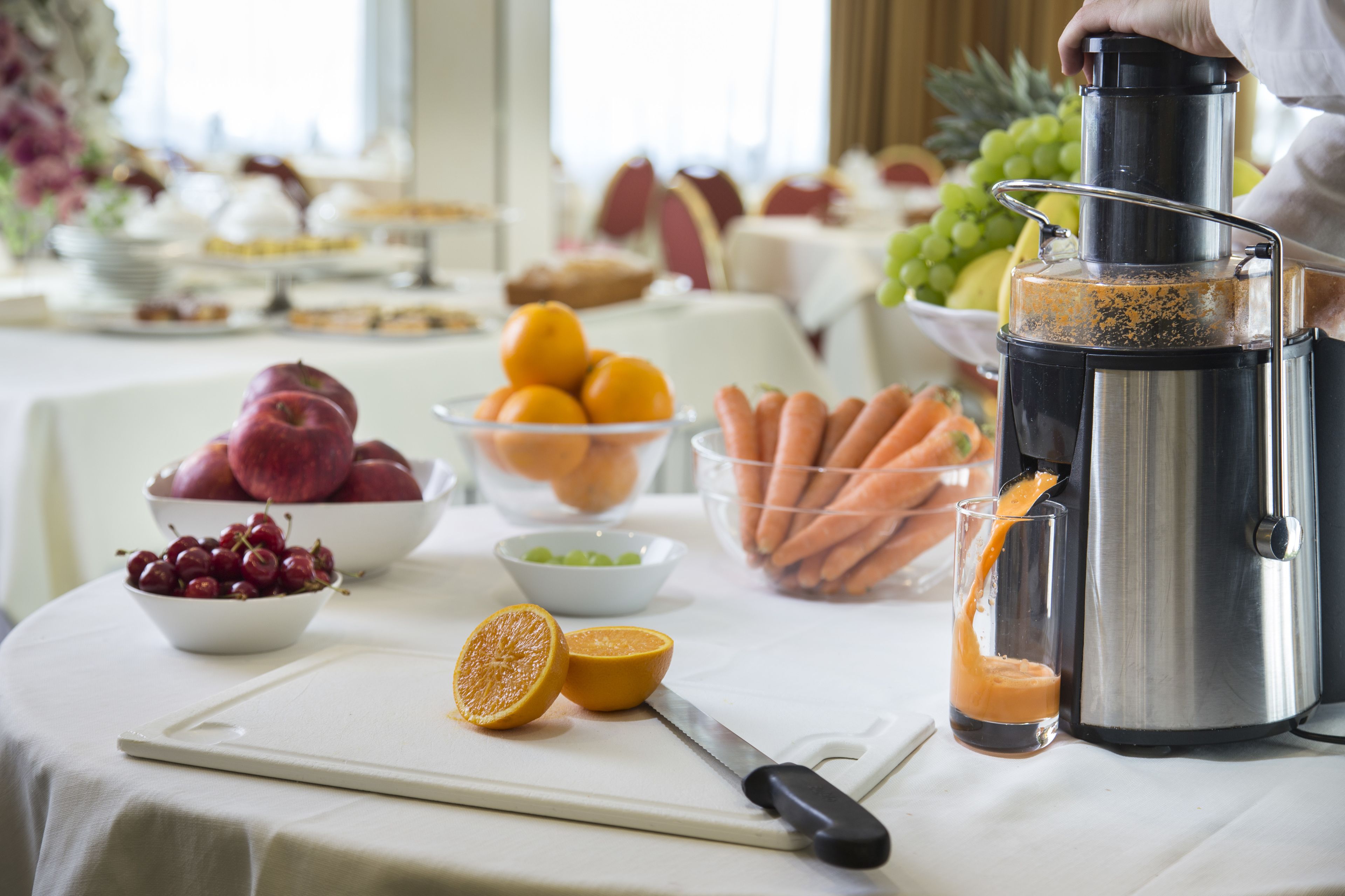 A table with a juicer, bowls of fruits, and a cutting board with a knife.
