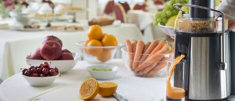 A table with a juicer, bowls of fruits, and a cutting board with a knife.