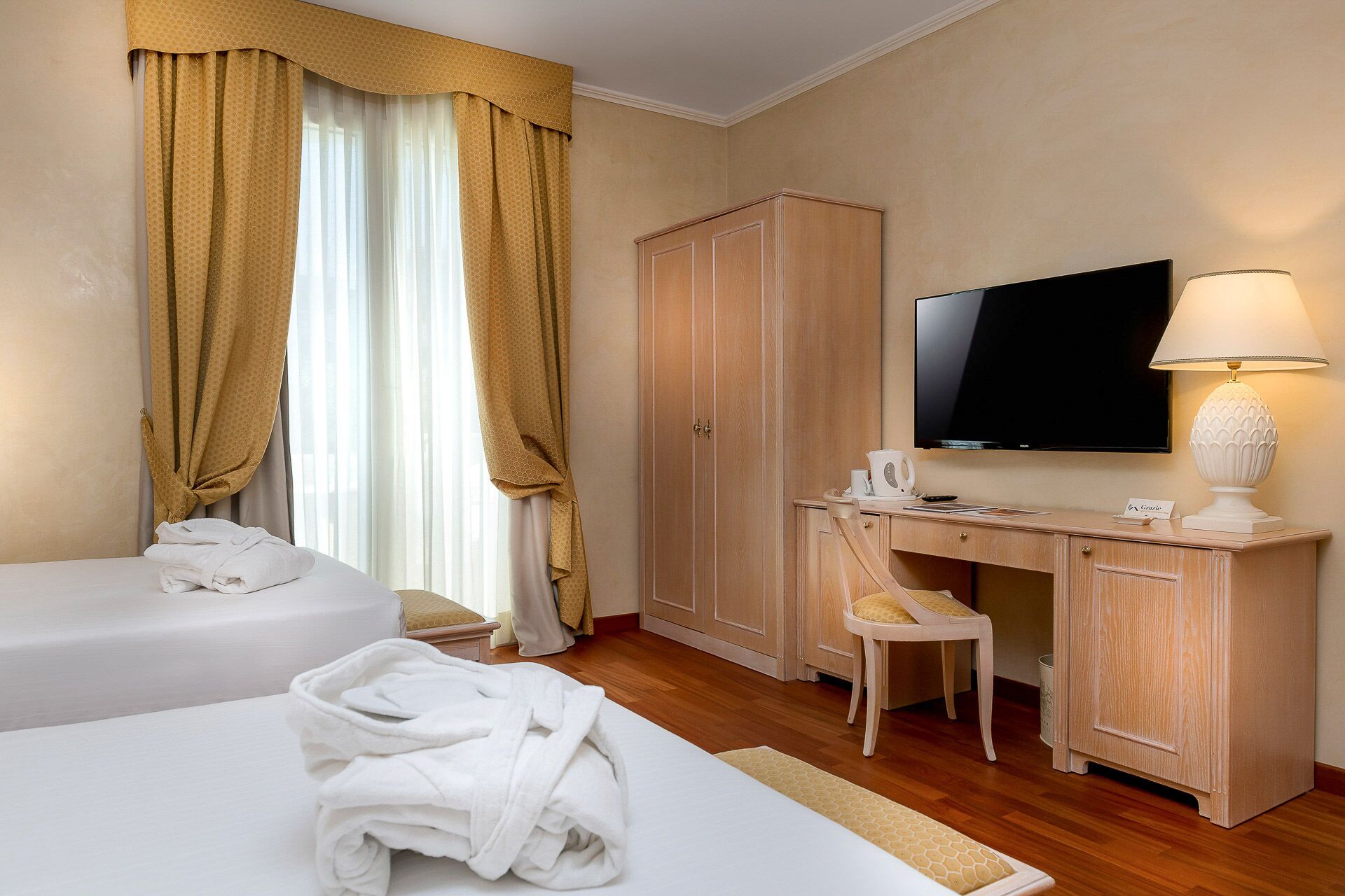 A hotel room with two beds, a desk, a television, and a lamp.