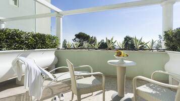 Una terraza con sillas de mimbre, una mesita redonda con un frutero y una toalla blanca colgada de una silla.