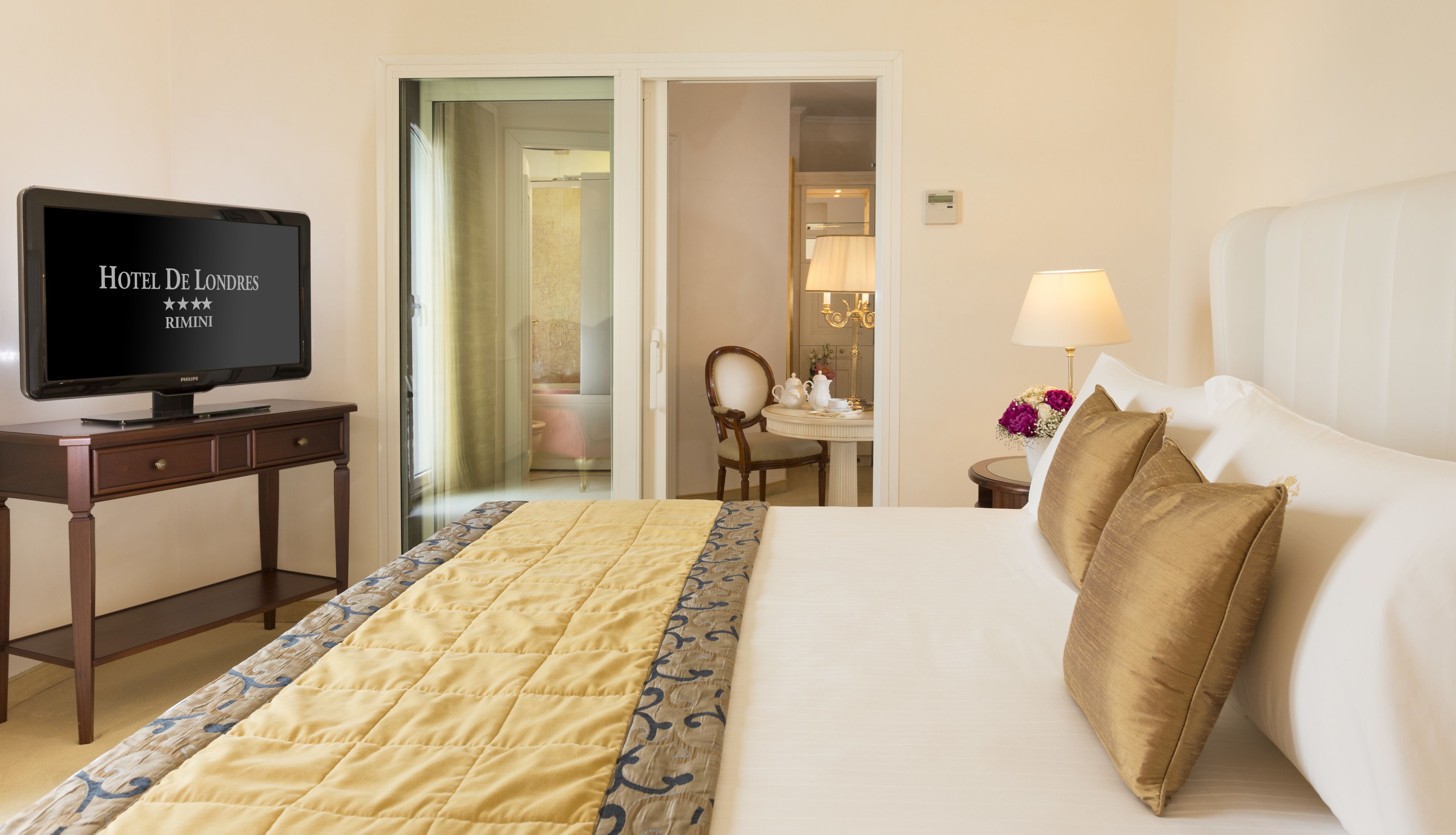 Une chambre d’hôtel avec un lit, une télévision, un bureau et une salle de bain, visibles à travers une porte ouverte.