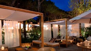Un área de patio al aire libre con mobiliario de madera, incluyendo sillas y mesas, bajo toldos blancos.