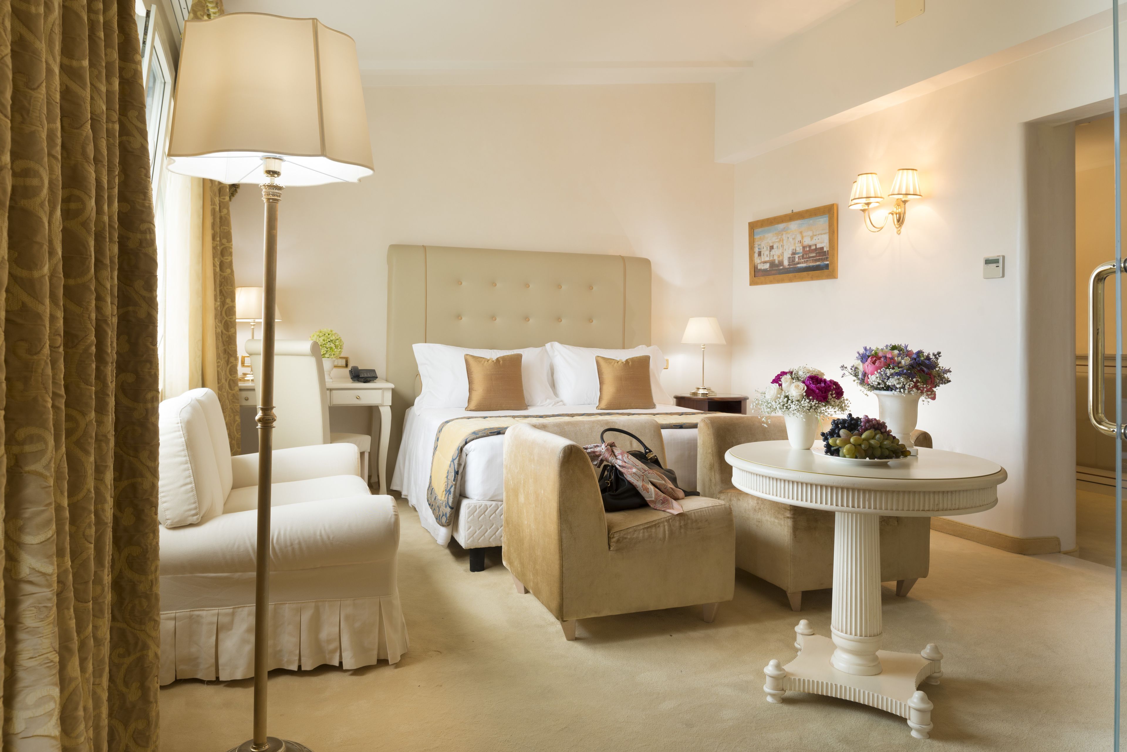 Una habitación de hotel con cama, una silla, una mesa con flores y una lámpara.