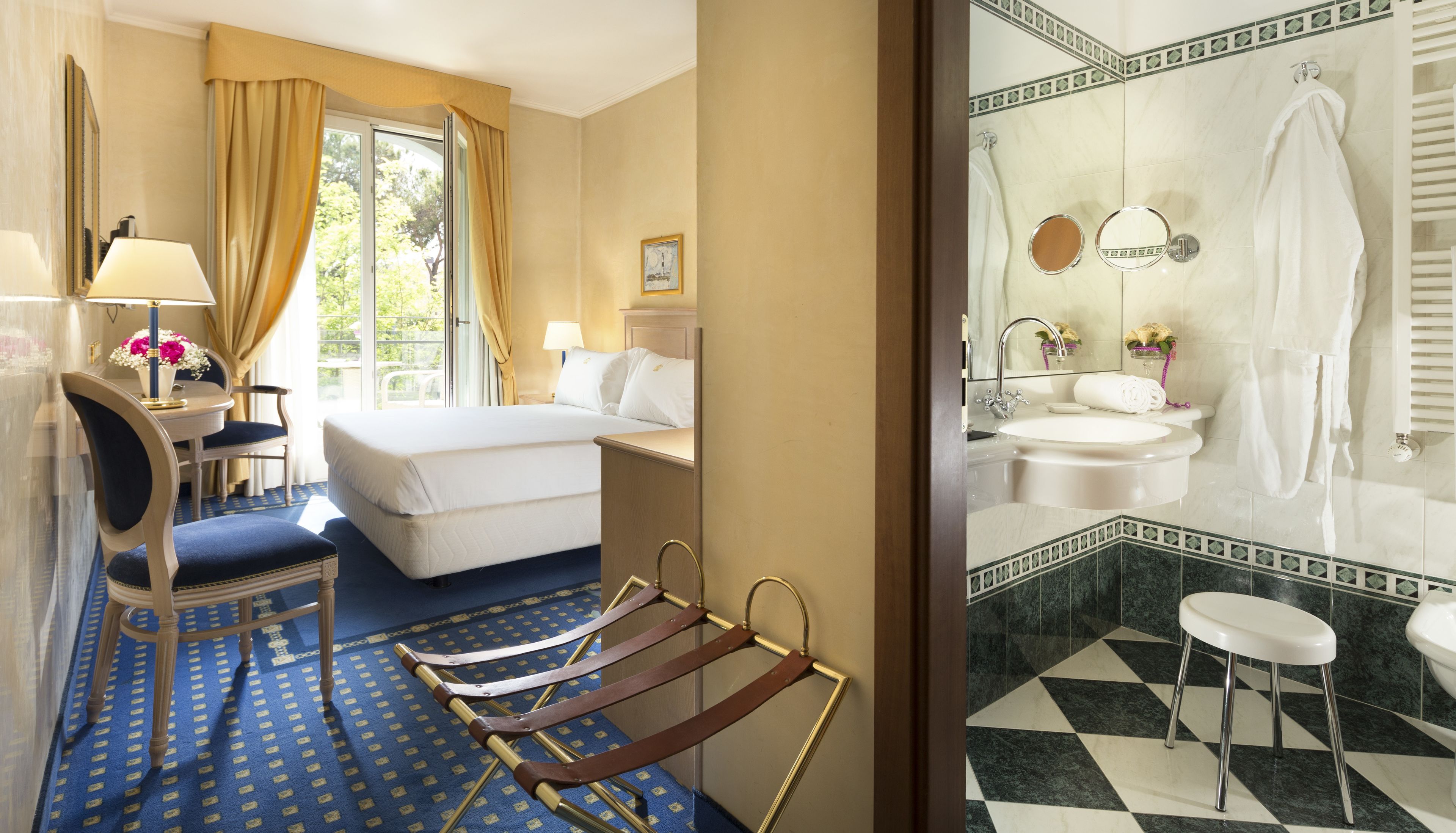 Hotelkamer met een bed, bureau, stoel, raam met gordijnen, badkamer met wastafel, spiegel en toilet.