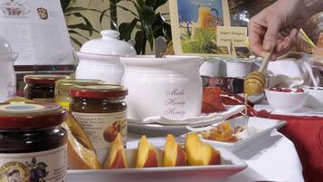 A table with various food items including jars of preserves, a bowl of honey, and a plate of fruit.