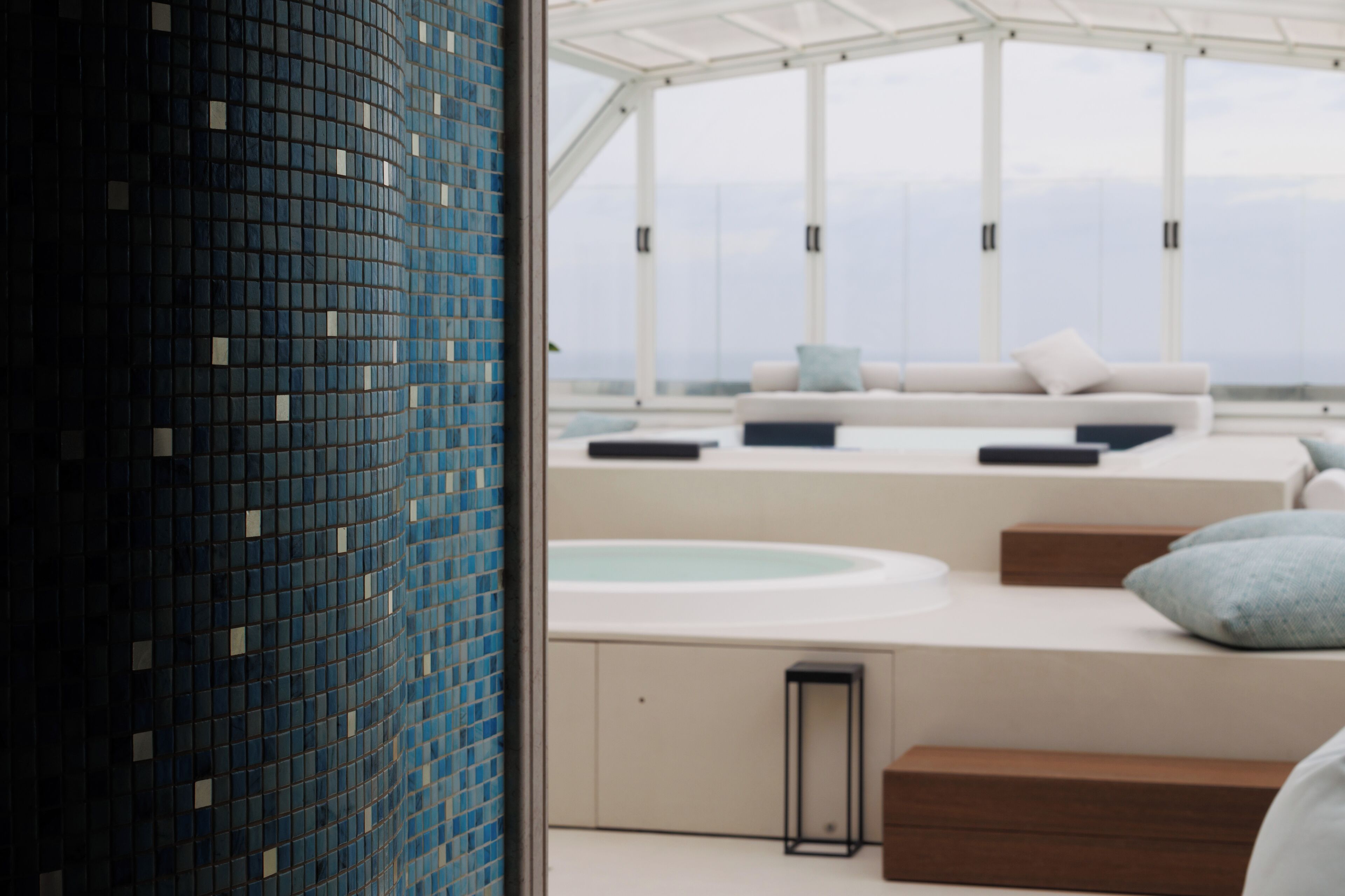 A modern interior with a glass wall, a seating area with a sofa and cushions, and a built-in hot tub.