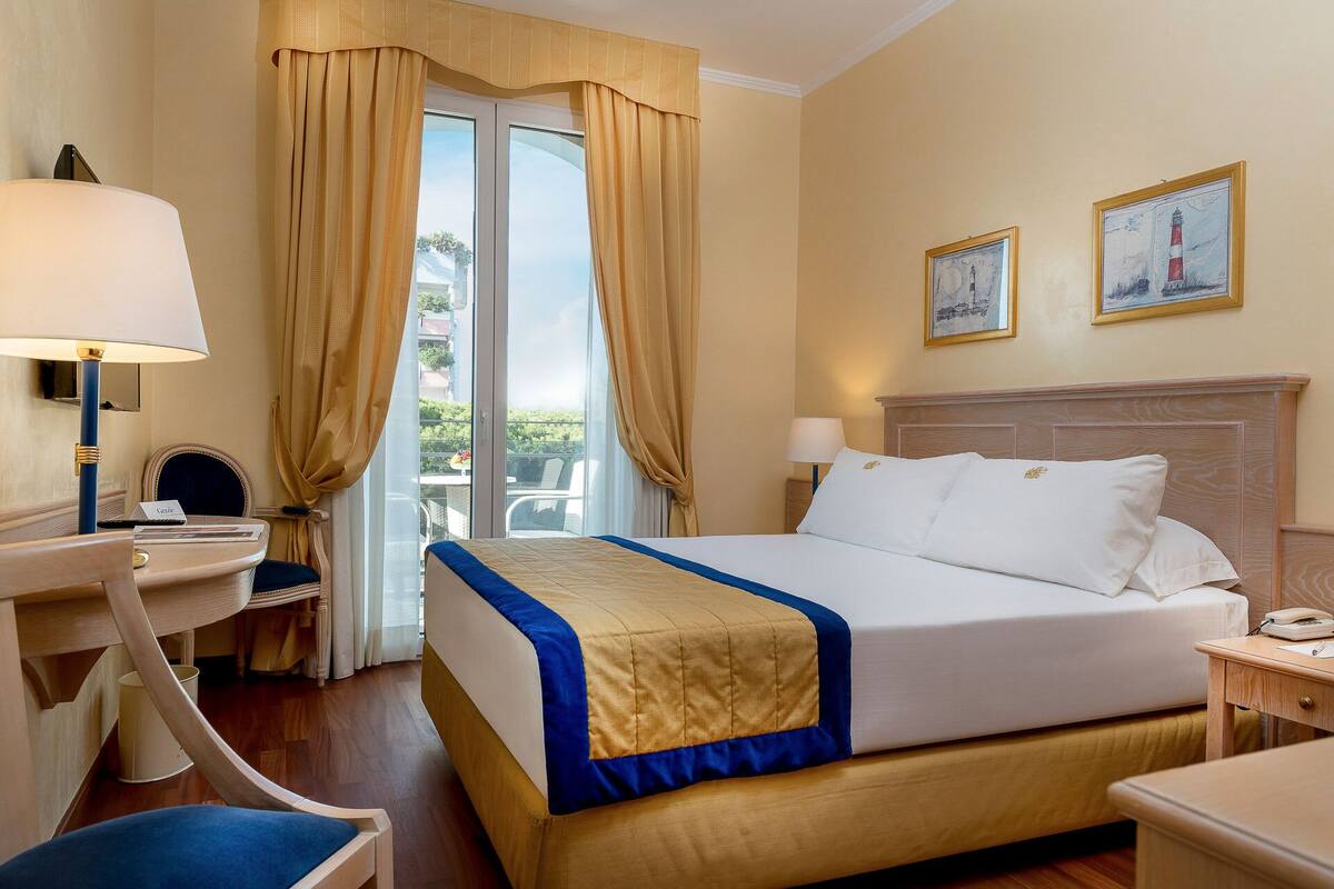 Ein Hotelzimmer mit Bett, Schreibtisch, Stuhl, Lampe und zwei Bildern an der Wand.