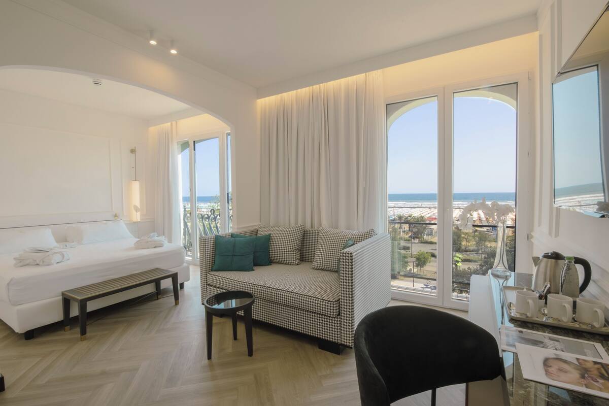 Ein modernes Hotelzimmer mit Bett, Sofa, Essbereich und großen Fenstern mit Blick auf die Stadt.