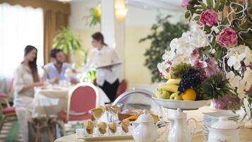 A dining table set with a fruit bowl, pastries, a pitcher, and a vase of flowers.