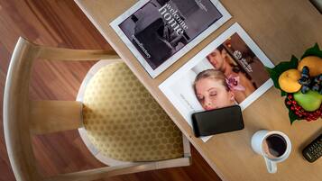 A table with a magazine, a smartphone, a remote control, a cup of coffee, and a fruit arrangement.