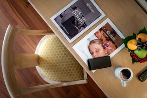 Un tavolo con una rivista, uno smartphone, un telecomando, una tazza di caffè e un cestino di frutta.