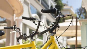 Uma bicicleta amarela com a inscrição "HOTEL DE LONDRES", estacionada em frente a um prédio com varandas.