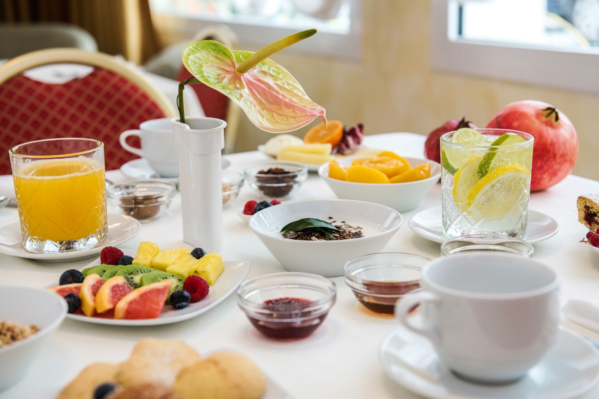 Een ontbijttafel met verschillende soorten fruit, een karaf, een glas sinaasappelsap en een kop koffie.