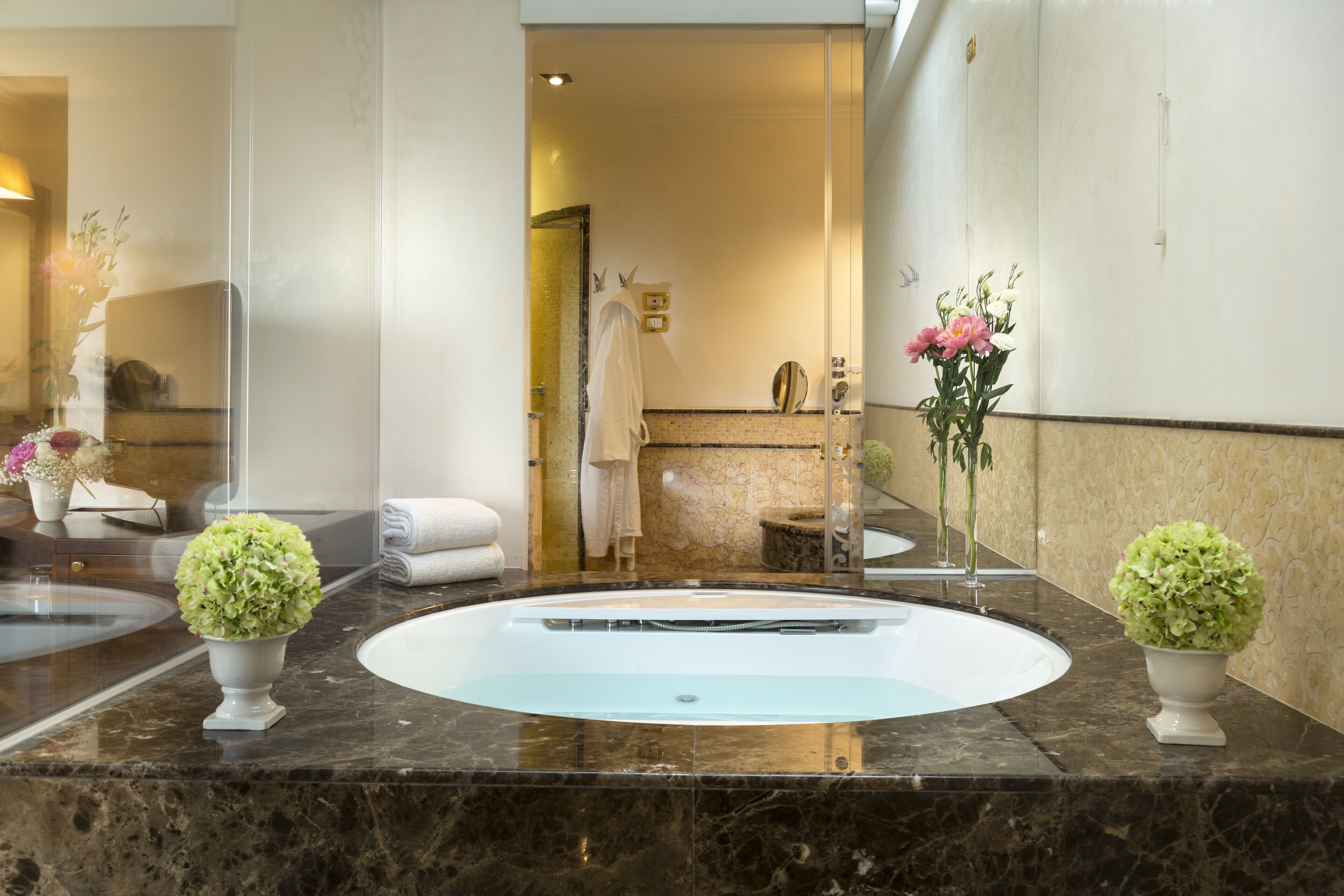 Une salle de bain moderne avec deux vasques, des plans de travail en marbre et des vases décoratifs ornés de fleurs.