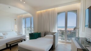 Habitación de hotel moderna con una cama grande, un banco, un escritorio de vidrio y vistas a la ciudad a través de amplios ventanales.